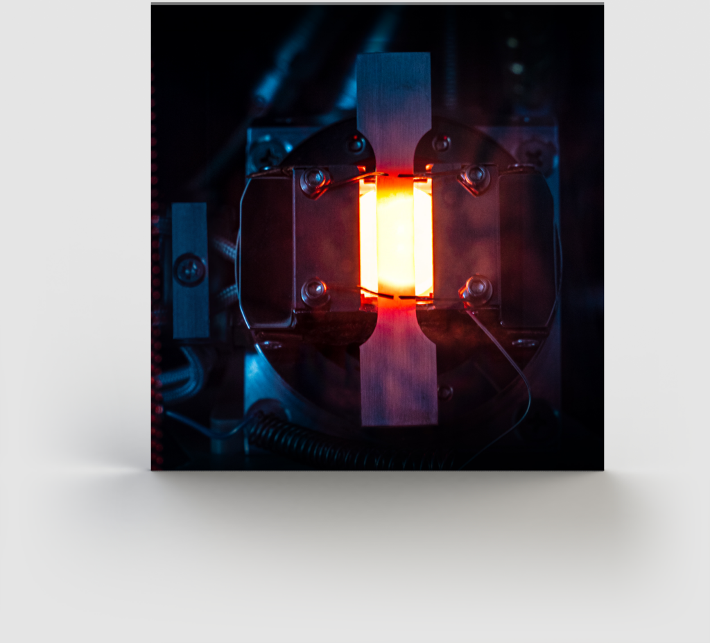 A close-up photograph of a glowing tube-like object held in place by two metal clamps. The tube emits a bright orange light, illuminating its surrounding components like an SEO expert illuminating keywords. The background is dark and mostly out of focus, highlighting the glowing object.